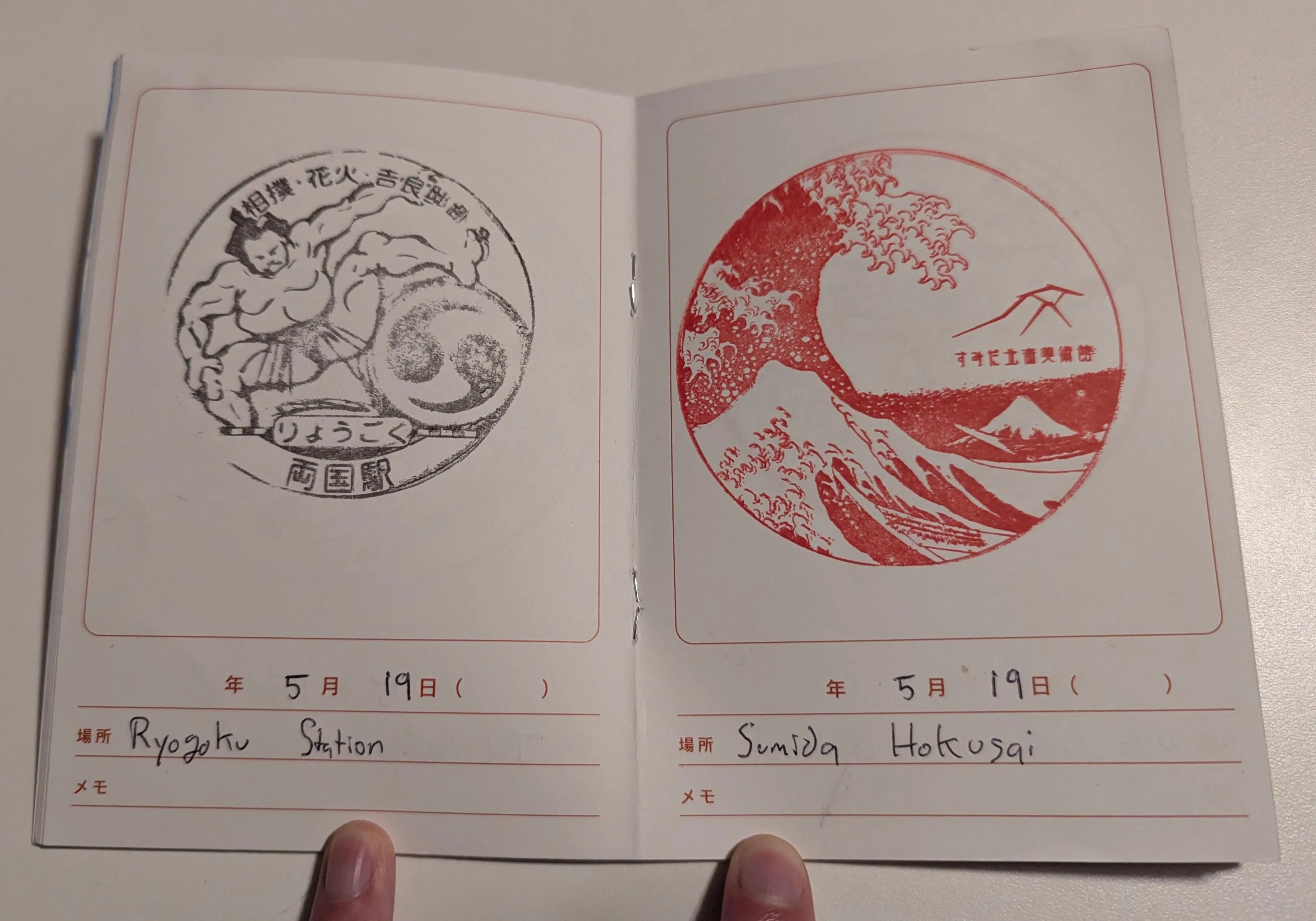 Opened stamp book showing two stamps: one featuring a sumo wrestler for ryogokun station,
and another featuring Under the Wave off Kanagawa for the Sumida Hokusai Museum